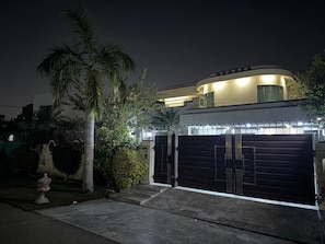 A modern house with a curved roof, a gated garage, and a well-maintained garden with palm trees.