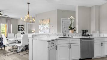Une cuisine moderne avec des meubles blancs, un îlot central et un coin repas avec des chaises blanches.