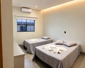 A hotel room with two beds, a window with a view, an air conditioning unit, and a small table.