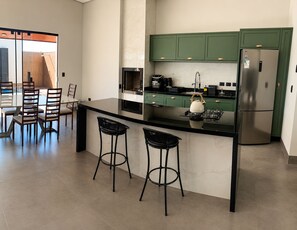 A modern kitchen with a central island, bar stools, green cabinets, and a stainless steel refrigerator.