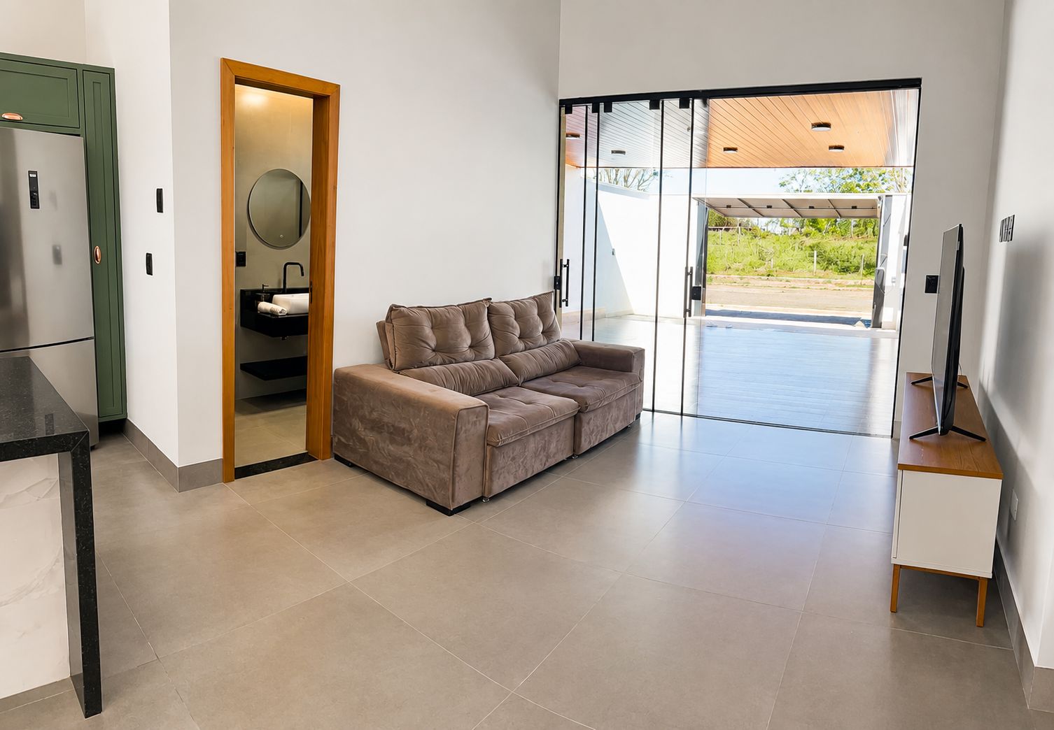 A modern interior with a sofa, a kitchen area, and a sliding glass door leading to an outdoor space.