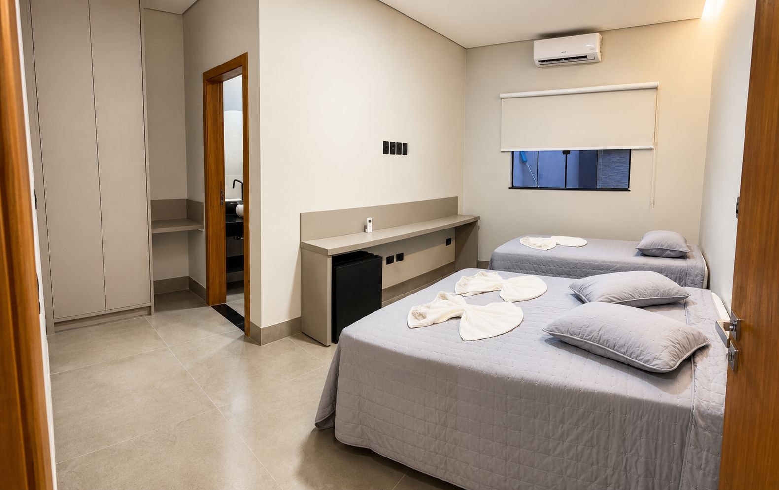 Una habitación de hotel con dos camas, un escritorio pequeño, un espejo y un armario.