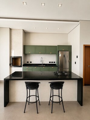 A modern kitchen with green cabinets, a black countertop, and two black bar stools.