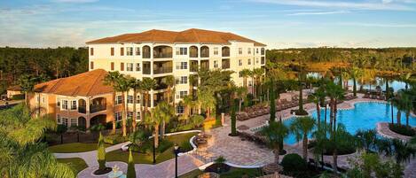 A resort with a large pool, palm trees, and a multi-story building with balconies.