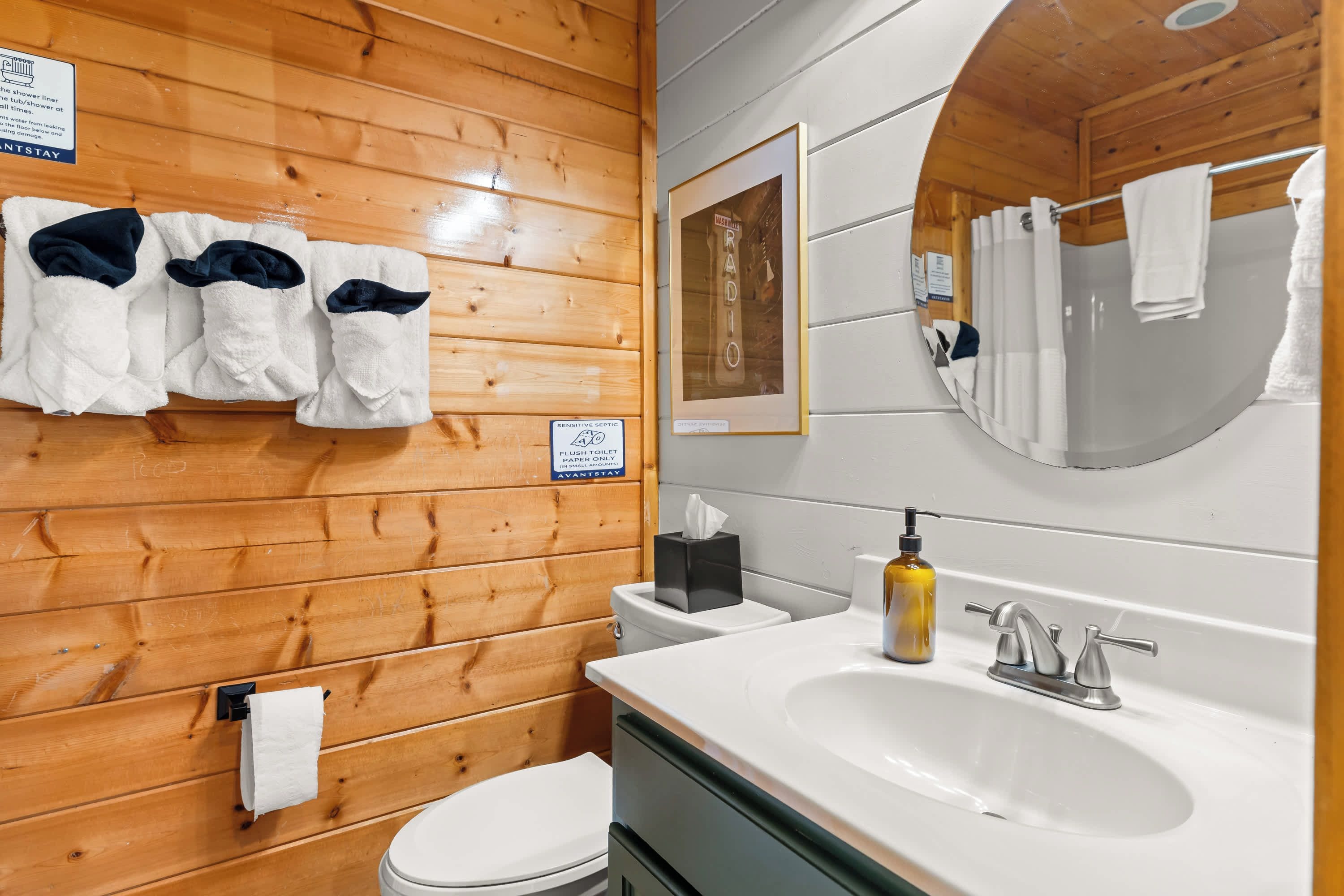 A wooden cabin bathroom with a toilet, sink, and a mirror. There are towels hanging on the wall and a sign indicating the use of the toilet.