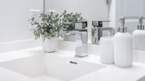 Ein modernes Badezimmer mit einem weißen Waschbecken, einem Chromarmaturen und einem Blumentopf.