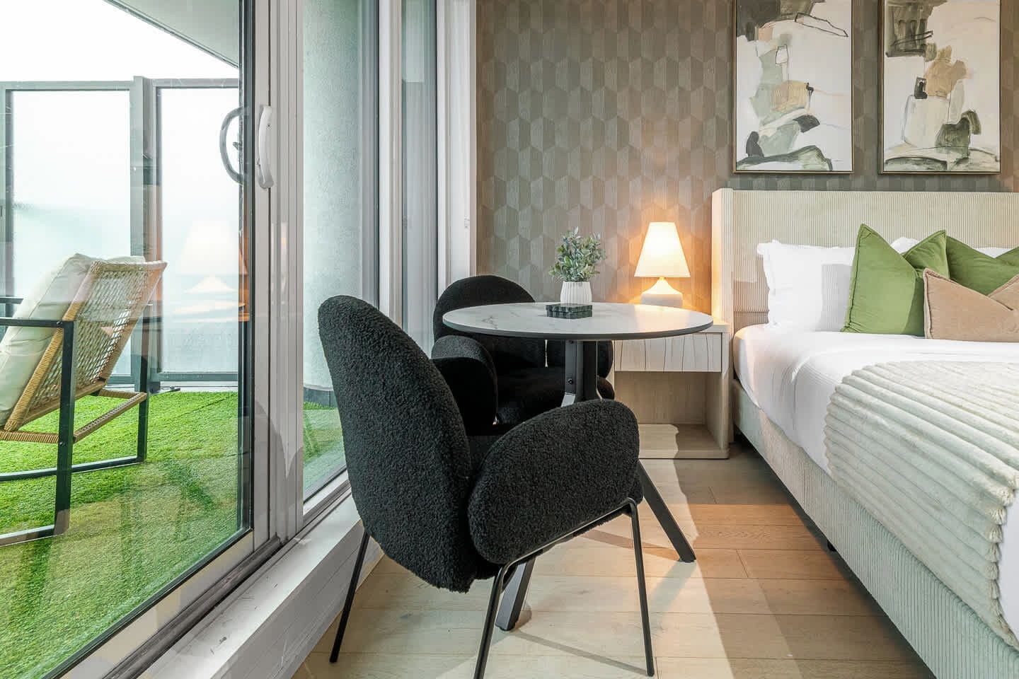 Une chambre d’hôtel avec un lit, une petite table avec des chaises, une table de chevet avec une lampe et une vue sur l’extérieur grâce à une grande fenêtre.