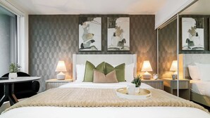 Ein Hotelzimmer mit einem großen Bett, zwei Nachttischen mit Lampen, einem Sessel und abstrakter Wandkunst.