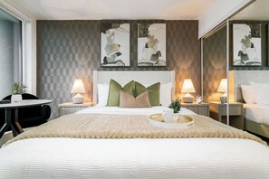 Ett hotellrum med en stor säng, två sängbord med lampor, en stol och abstrakt konst på väggen.