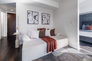 A modern bedroom with a white sofa, a brown throw blanket, and abstract wall art.