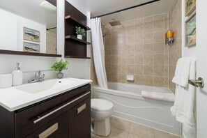 A bathroom with a bathtub, toilet, and sink. There are shelves with plants and a mirror above the sink.