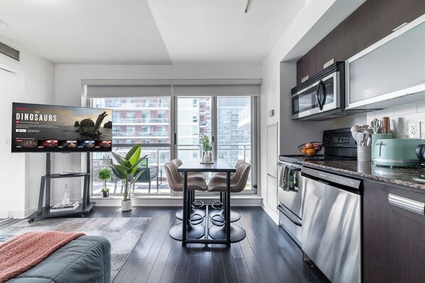 A modern kitchen with a dining area, large windows, and a flat-screen TV.