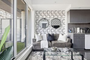 A modern living room with a glass coffee table, grey sofa, and a patterned wall.
