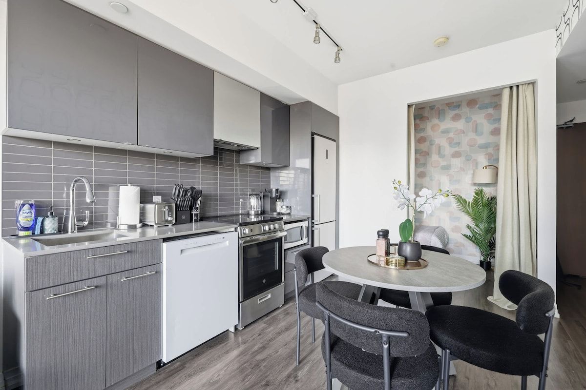 A modern kitchen with grey cabinets, a built-in oven, and a round dining table with four chairs.