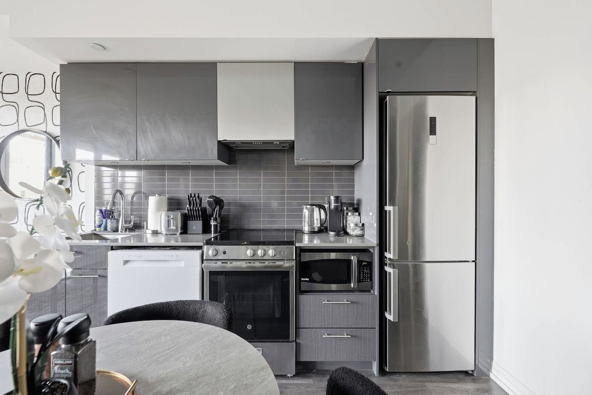 A modern kitchen with stainless steel appliances, grey cabinetry, and a white tiled backsplash.