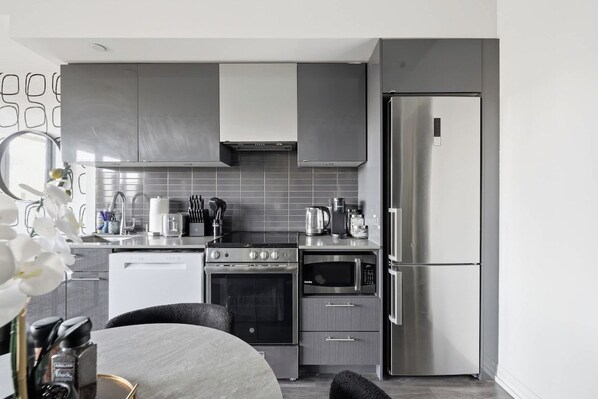 A modern kitchen with stainless steel appliances, grey cabinetry, and a white tiled backsplash.