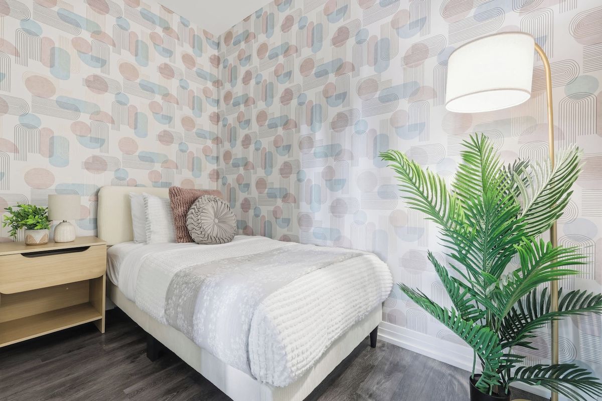 Un dormitorio con cama, mesita de noche, lámpara y una planta en maceta.