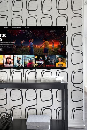 Ein flachbildfernseher an einer Wand mit geometrischem Muster, der eine Auswahl an Filmen zeigt.