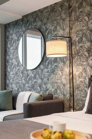 A hotel room with a bed, a round mirror, a floor lamp, and a floral wallpaper. - Downtown Studio w Balcony Steps to Eaton Centre | Parking Available (Toronto)