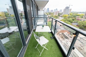 A balcony with a glass railing, a table, chairs, and a small potted plant. - Downtown Studio w Balcony Steps to Eaton Centre | Parking Available (Toronto)
