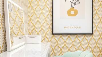 A bathroom with a white vanity, a framed botanical print on the wall, and a mint green chair.