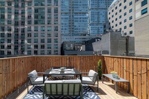 Une terrasse sur le toit avec une table à manger pour quatre personnes, entourée de rampes en bois et agrémentée d’un tapis à motifs.