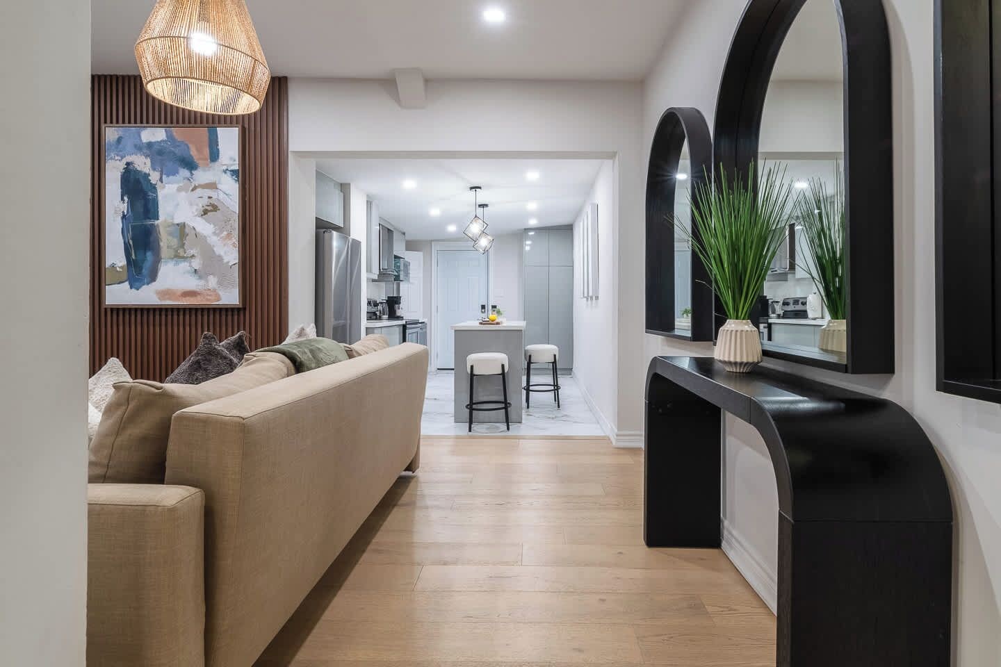 A modern interior with a sofa, dining area, kitchen, and a hallway leading to a mirrored wall.