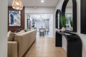 Un intérieur moderne comprenant un canapé, un coin repas, une cuisine et un couloir menant à un mur recouvert de miroirs.