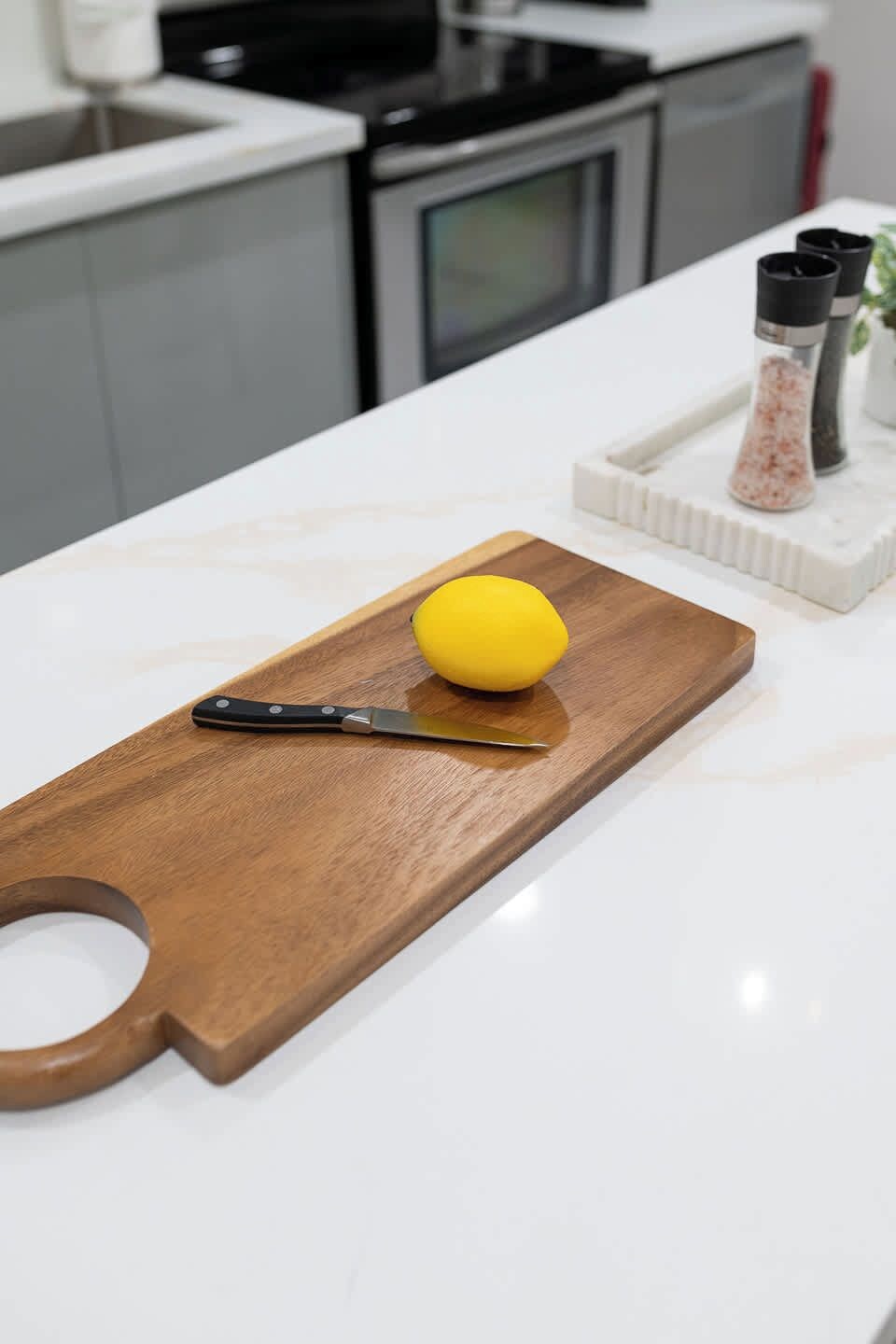Uma bancada de cozinha com tábua de corte de madeira, uma faca e um limão.