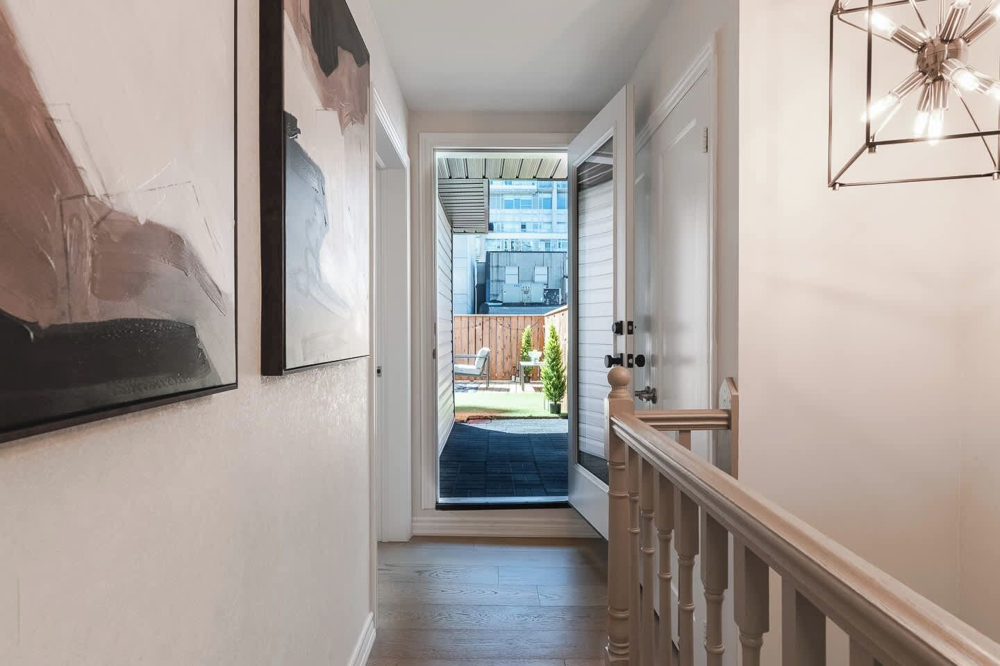 A hallway with a door leading to a covered outdoor area, a staircase with a wooden handrail, and a framed picture on the wall.