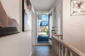 A hallway with a door leading to a covered outdoor area, a staircase with a wooden handrail, and a framed picture on the wall. - Two king beds + huge private patio (Toronto)