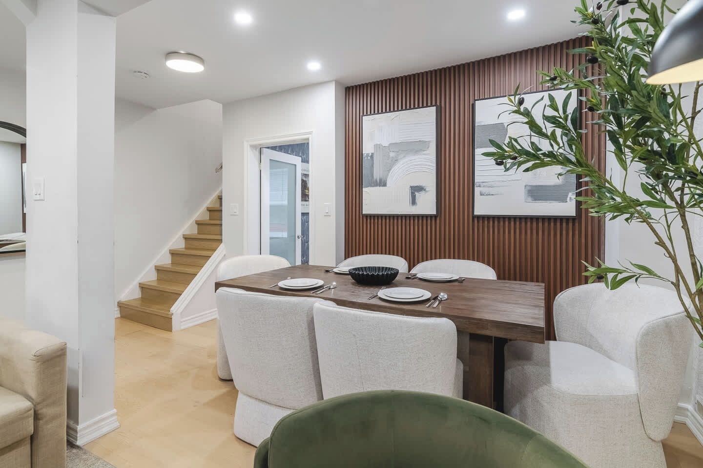 A dining area with a wooden table, white chairs, and a staircase in the background.