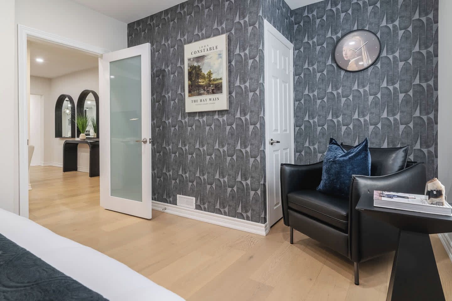 A modern living room with a black leather sofa, a round clock, and a framed picture on the wall.