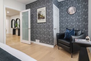 A modern living room with a black leather sofa, a round clock, and a framed picture on the wall. - Two king beds + huge private patio (Toronto)