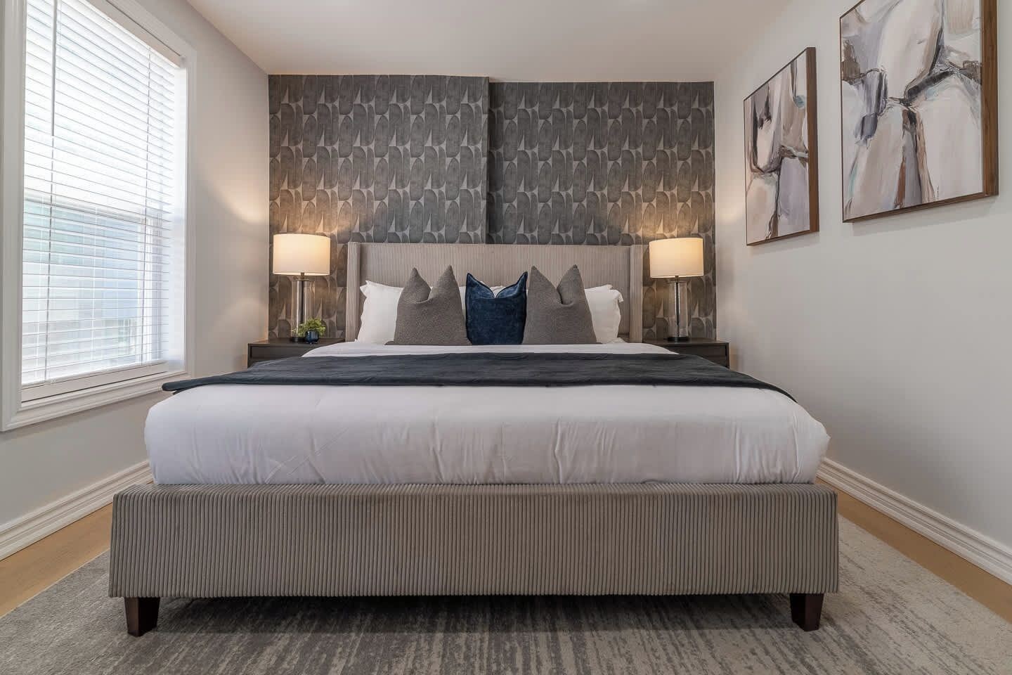 A hotel room with a large bed, two bedside lamps, a window with blinds, and a textured wall.