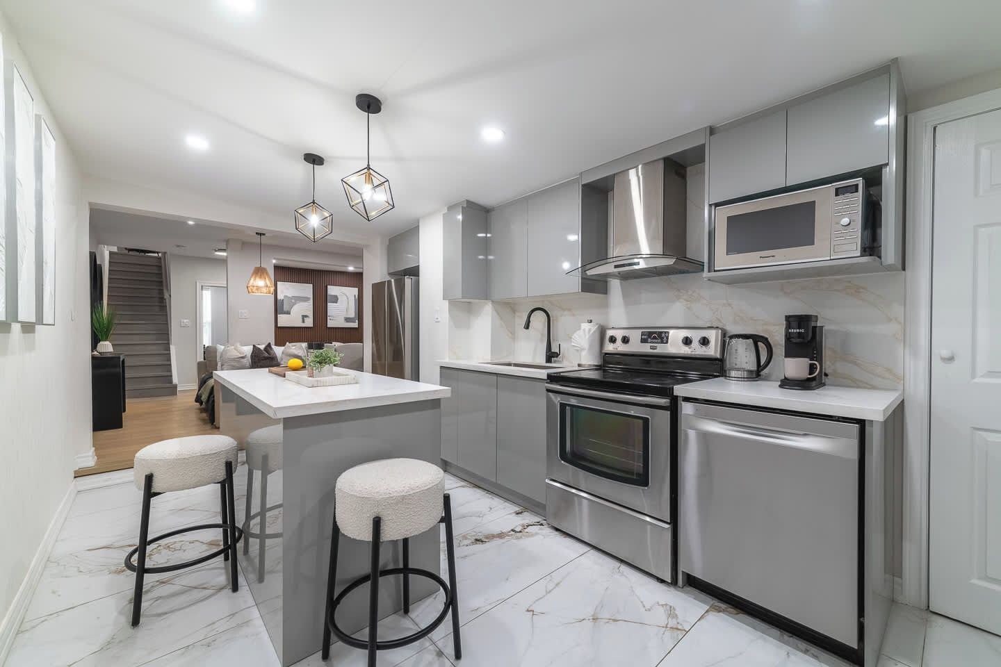 A modern kitchen with stainless steel appliances, a central island with stools, and pendant lighting.