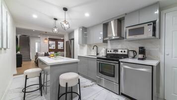 A modern kitchen with stainless steel appliances, a central island with stools, and pendant lighting.