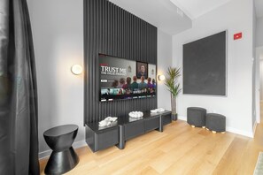 A modern interior with a flat-screen TV mounted on a wall, a seating area with ottomans, and a potted plant. - 3BR Downtown Toronto Stay near Chinatown & Kensington Market (Toronto)