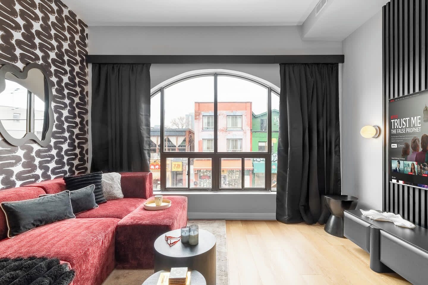 A modern living room with a red sofa, a large window, and a TV on the wall.
