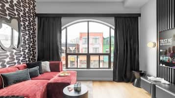 A modern living room with a red sofa, a large window, and a TV on the wall.
