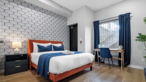 Une chambre d’hôtel avec un lit, un bureau, une chaise, une table de chevet et une fenêtre avec des rideaux.