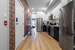 A modern kitchen with stainless steel appliances, a wooden floor, and a patterned wallpaper on the left wall. - 3BR Downtown Toronto Stay near Chinatown & Kensington Market (Toronto)