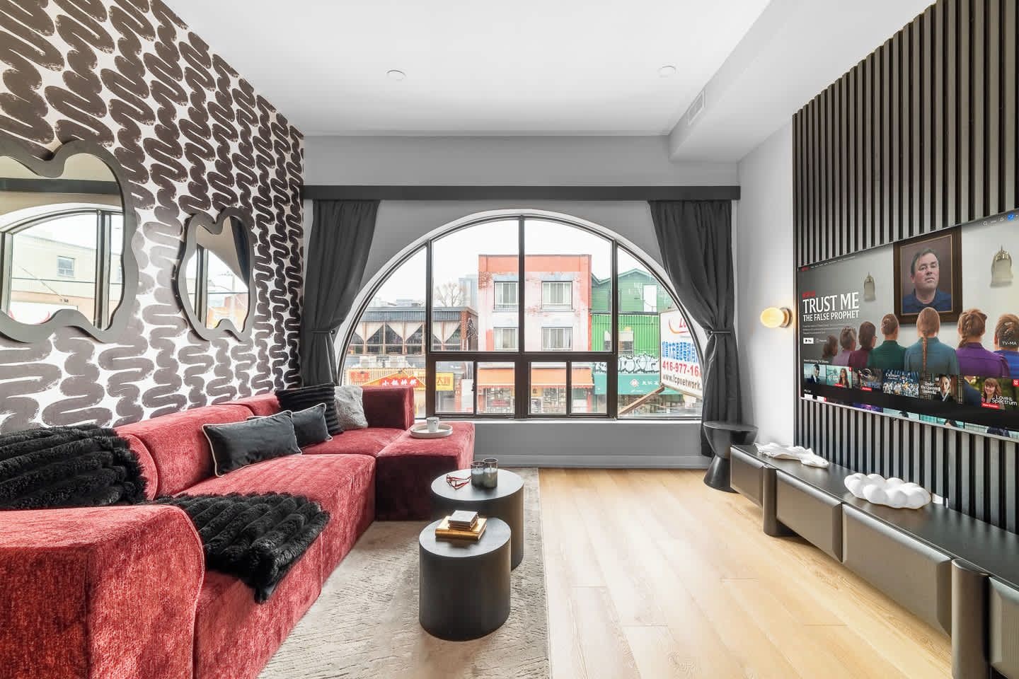 A modern living room with a red sofa, a round coffee table, and a large window offering a view of buildings outside.