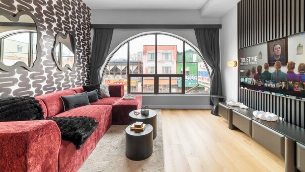 Un salon moderne avec un canapé rouge, une table basse ronde et une grande fenêtre donnant sur les bâtiments environnants.