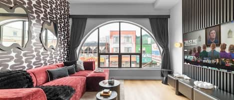 A modern living room with a red sofa, a round coffee table, and a large window offering a view of buildings outside.