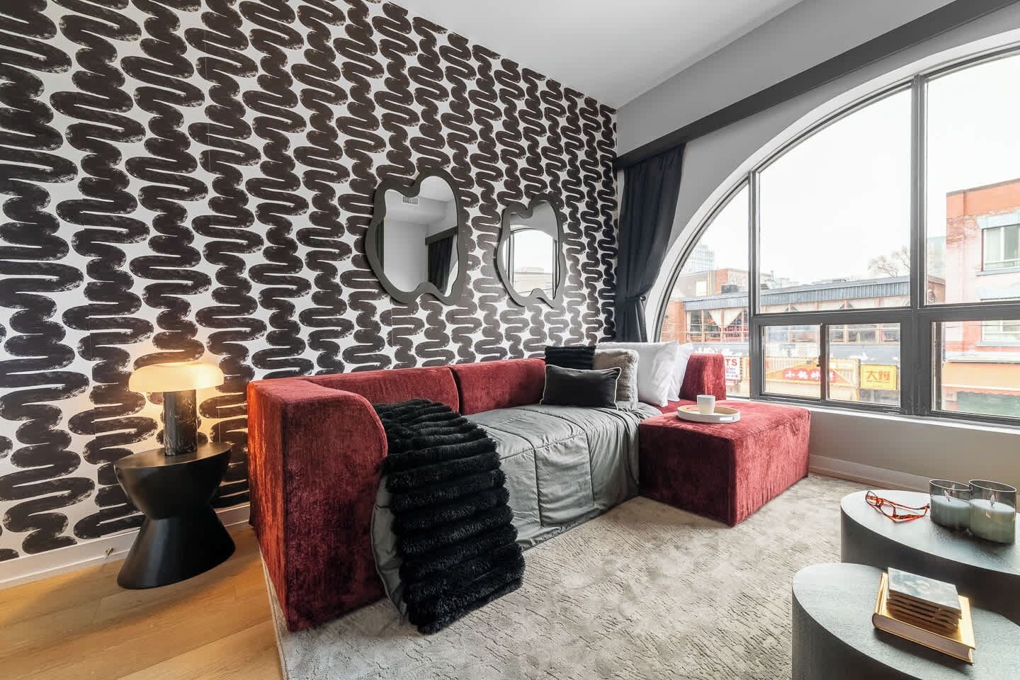 A modern living room with a unique black and white patterned wall, a large window with a view, a red sofa, and a small round table with books.