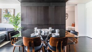 Un comedor moderno con un panel de madera oscura, una mesa de vidrio y sillas de madera.