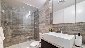 Un baño moderno con ducha envuelta en vidrio, un lavabo blanco y un inodoro.