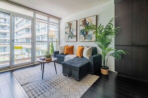 A modern living room with a sofa, ottoman, and a potted plant. - Sunlit Urban Studio Loft Sleeps 6 Luxe Stay (Toronto)