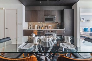 A modern kitchen with dark wood cabinets, stainless steel appliances, and a glass dining table set for six. - Sunlit Urban Studio Loft Sleeps 6 Luxe Stay (Toronto)